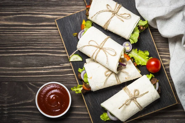 Burritos envolturas de tortilla con carne de res y verduras en respaldo de madera —  Fotos de Stock