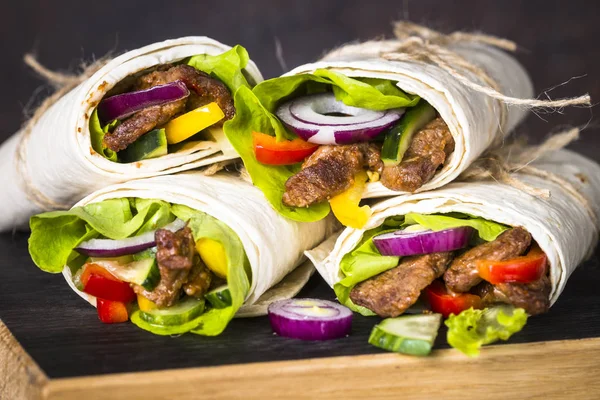 Burritos tortilla wraps with beef and vegetables on wooden close