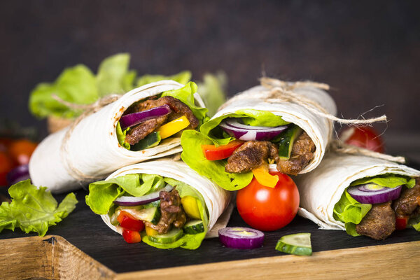 Burritos tortilla wraps with beef and vegetables on wooden close
