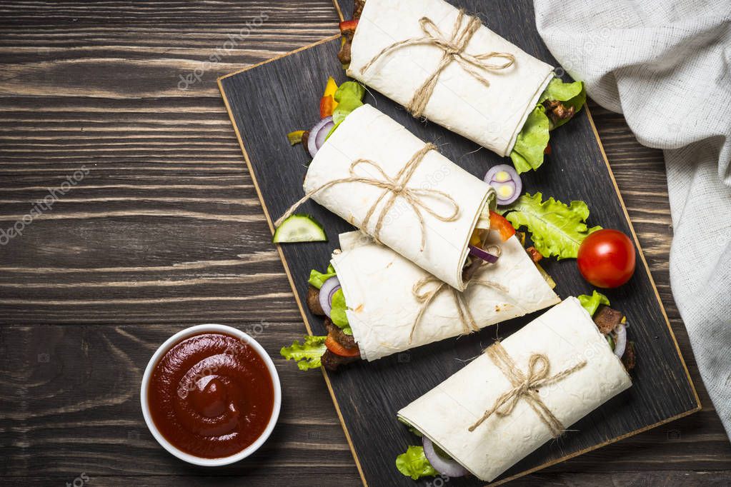 Burritos tortilla wraps with beef and vegetables on wooden backg