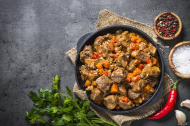 Beef stew with vegetables in iron pan on black. clipart