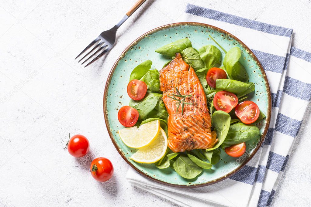 Baked salmon fish fillet with fresh salad top view on white.