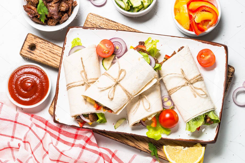 Burritos tortilla wraps with beef and vegetables on white background.