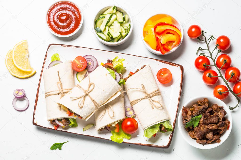 Burritos tortilla wraps with beef and vegetables on white background.