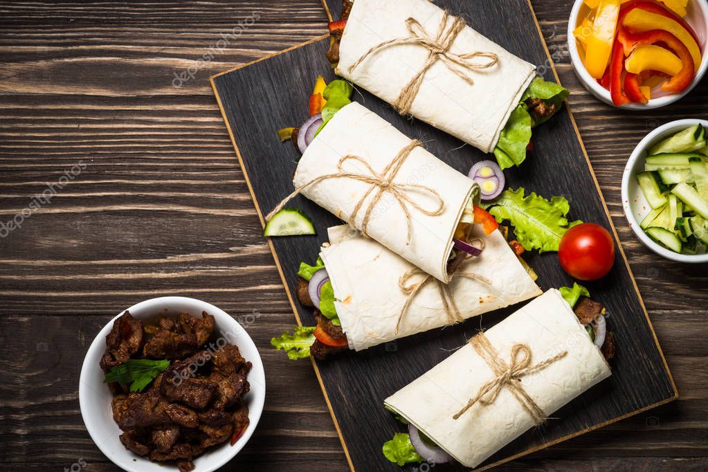 Burritos tortilla wraps with beef and vegetables on wooden background.