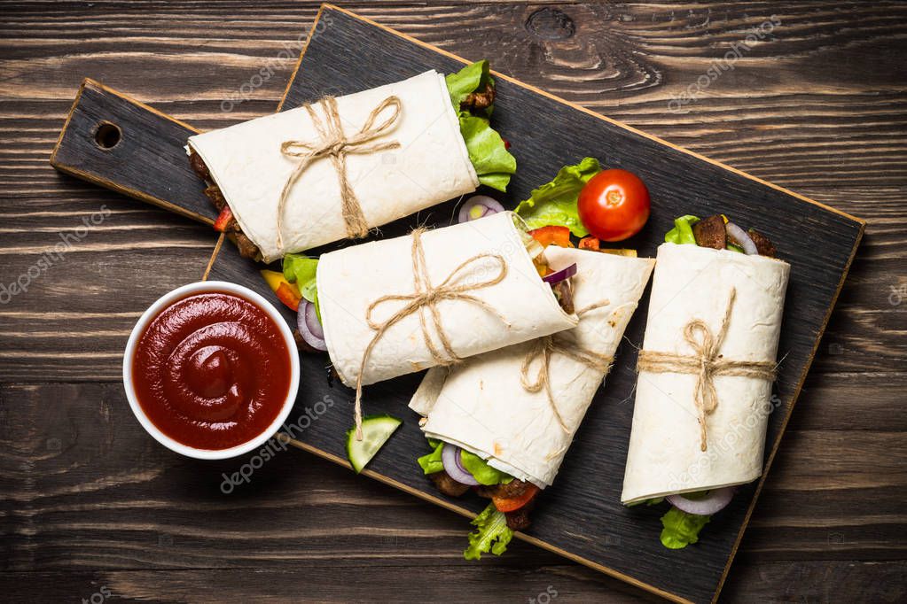 Burritos tortilla wraps with beef and vegetables on wooden background.