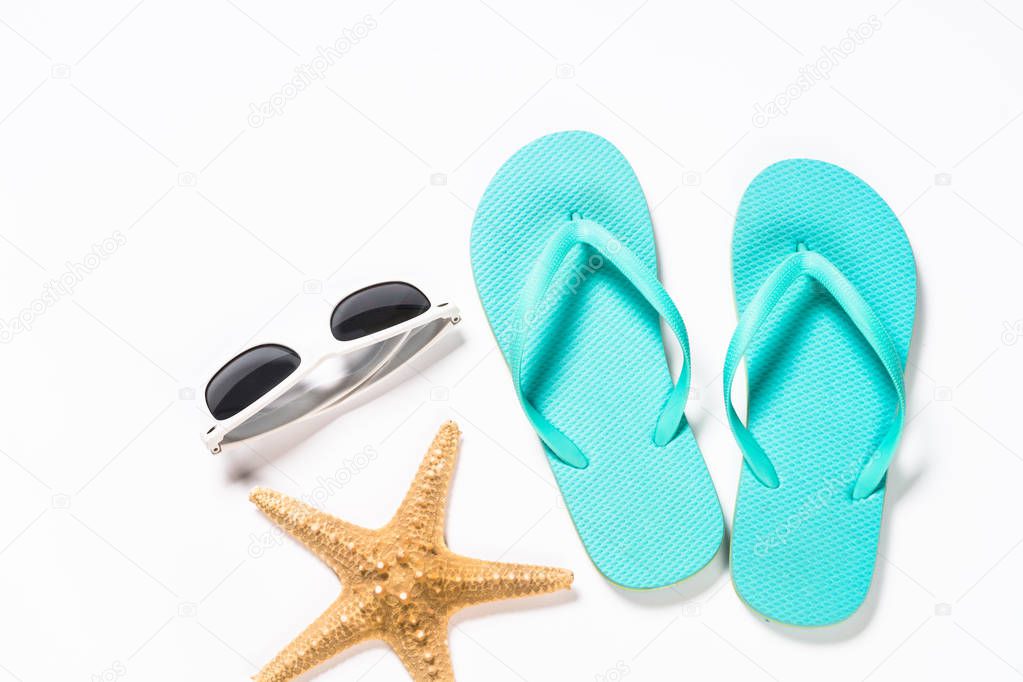 Blue flip flops, sunglasses and starfish on white background.