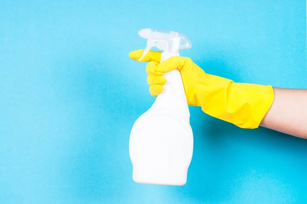 Mão em luvas amarelas segurar garrafa agente de limpeza no fundo azul . — Fotografia de Stock