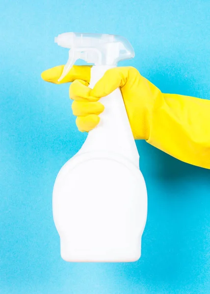 Main dans des gants jaunes tenir bouteille d'agent nettoyant sur fond bleu . — Photo