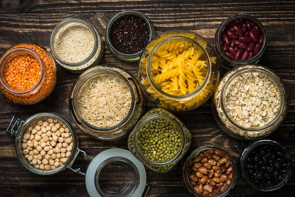 Cereali, legumi e fagioli in barattoli di vetro su tavolo di legno scuro . — Foto Stock