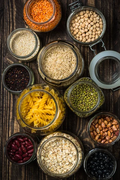 Granen, peulvruchten en bonen in glazen potten op donkere houten tafel. — Stockfoto