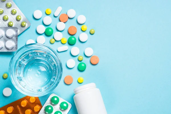 Tabletták és egy pohár víz a kék felülnézetben. — Stock Fotó