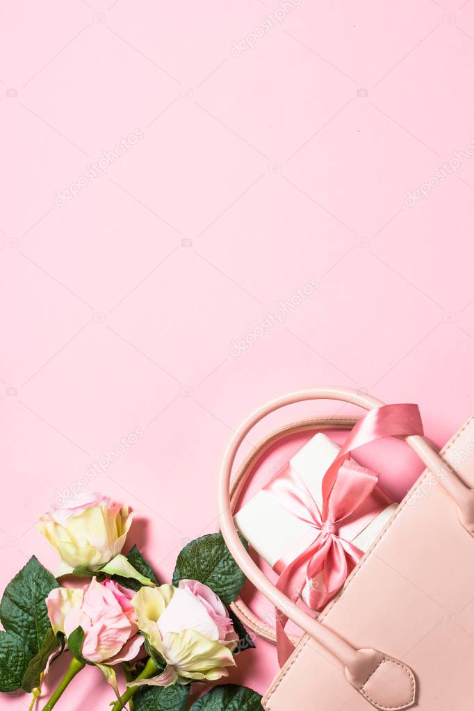 Woman flat lay background. Pink roses, handbag and present box on pink  background. Image toned, space for your text.