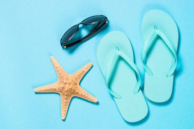 Mavi flip flop, güneş gözlüğü ve denizyıldızı mavi zemin üzerine.