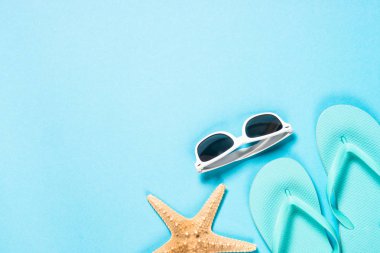 Mavi flip flop, güneş gözlüğü ve denizyıldızı mavi zemin üzerine.