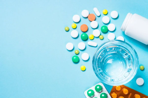 Tabletták és egy pohár víz a kék felülnézetben. — Stock Fotó