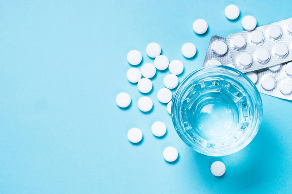 Tablety a sklenice s vodou na pohled s modrou barvou. — Stock fotografie