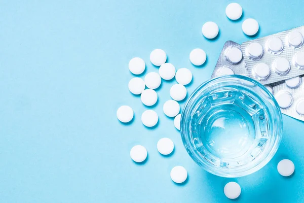 Tablety a sklenice s vodou na pohled s modrou barvou. — Stock fotografie