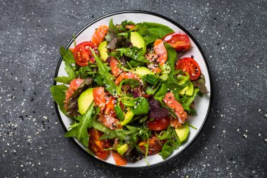 Siyah üst görünümde taze sebzeli somon salatası.