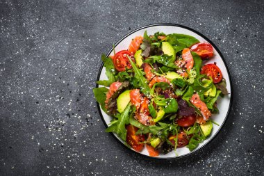 Siyah üst görünümde taze sebzeli somon salatası.