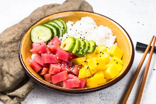 Tuna poke bowl with rice, avocado, mango and cucumber on white table.