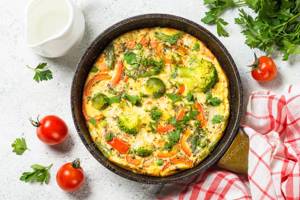 Frittata with vegetables on white stone table.