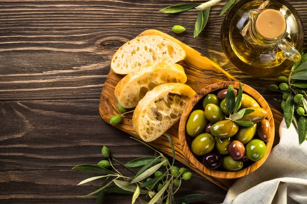 Oliwki, oliwa z oliwek i ciabatta na drewnianym stole. — Zdjęcie stockowe