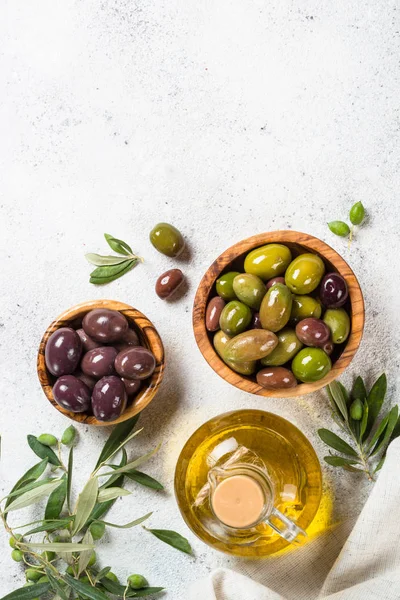 Olives in wooden bowls and olive oil bottle on white background. — Stock Photo, Image