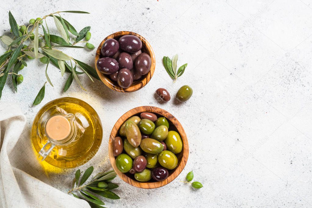 Olives in wooden bowls and olive oil bottle on white background.