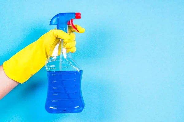 Sárga kesztyűt kezét tartsa tisztító ügynök üveg-kék háttér. — Stock Fotó