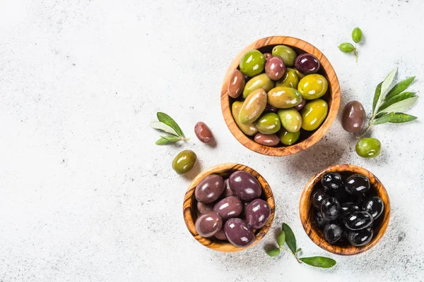 Natuurlijke Griekse olijven in houten kommen en olijfolie fles op witte achtergrond. — Stockfoto