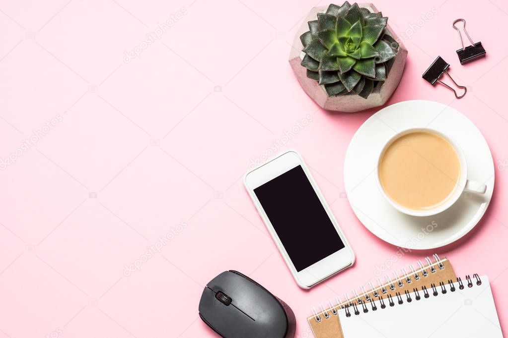 Office workplace with notepad, coffee cup and keyboard on pink background.