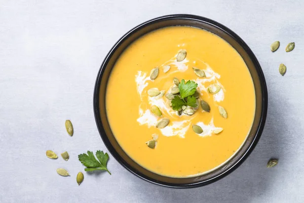 Pumpkin cream soup on light stone table.