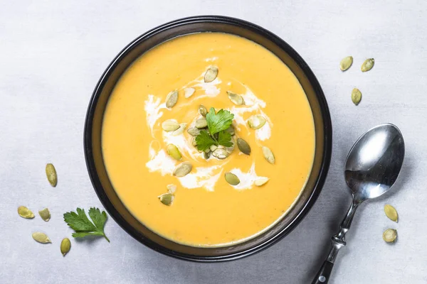 Pumpkin cream soup on light stone table.