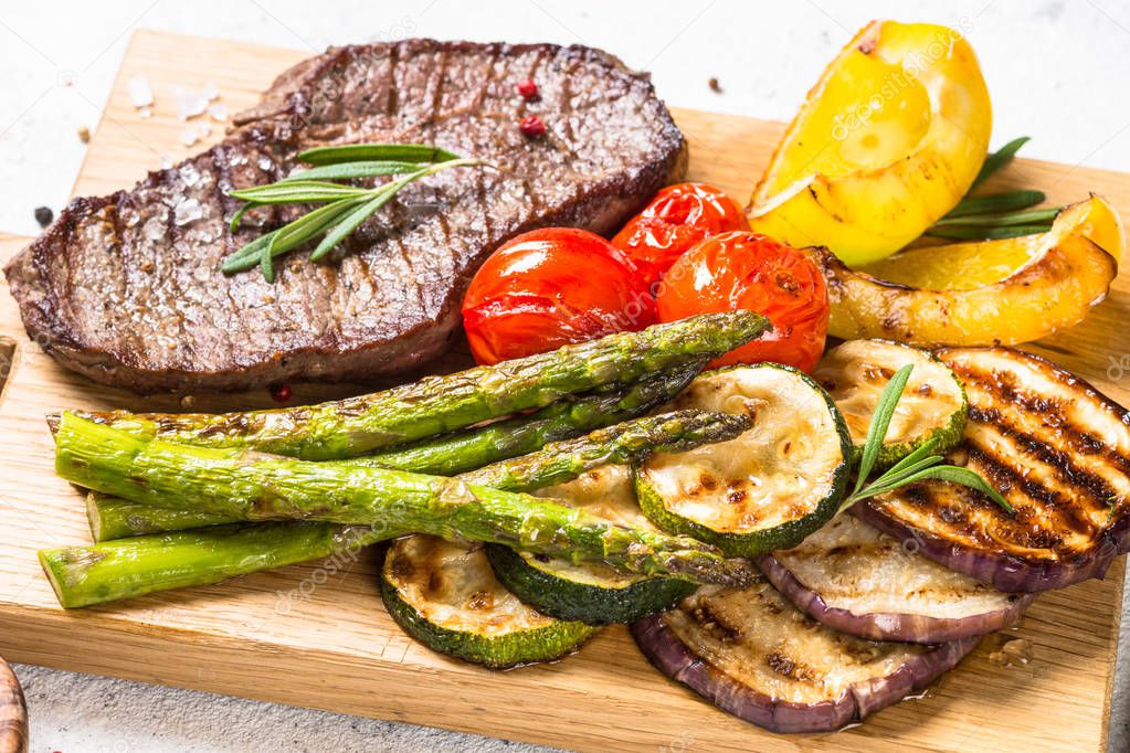 Beef steak grilled with vegetables on white stone table.