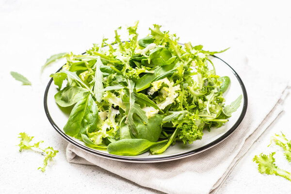 Green salad leaves mix on white table.