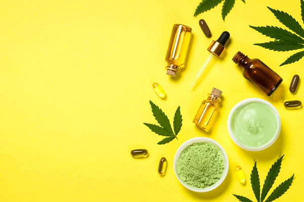 Kannabiszolaj és zöld levelek a sárga asztalnál. — Stock Fotó