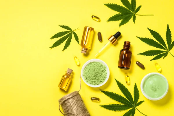 Cannabis oil and green leaves at yellow table. — Stock Photo, Image