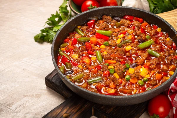 Chili con carne in skillet on light stone table.