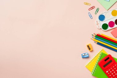 Okul malzemeleri renkli arka planda. Not defteri, kalemler, hesap makinesi ve diğerleri. Kopyalama alanı olan düz.