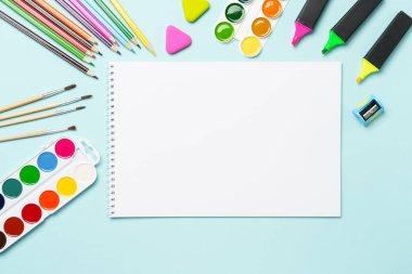 Çizim defteri, kalemler, suluboya boyalar ve mavi arka planda kalemler. Metin için alanı olan sanat yaratıcı bileşimi.