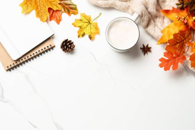 Beyaz arka planda sonbahar çalışma alanı. Not defteri, kahve kupası, rahat süveter ve sarı yapraklar. Metin için boşluk ile düz uzandı.