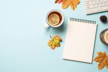 Sonbahar çalışma alanı düz arka planda yatıyordu. Dizüstü bilgisayar, defter, çay kupası, mavi arka planda örülmüş süveter..