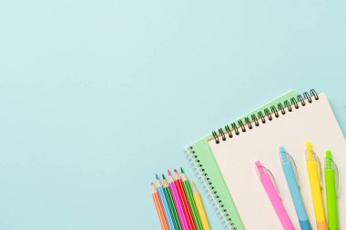 Not defteri, kalemler ve mavi arka planda renkli kalemler. Metin için boşluk ile düz uzandı.