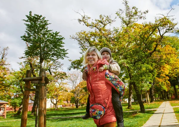 Kvinnan ger lite pojke piggyback ride leende — Stockfoto