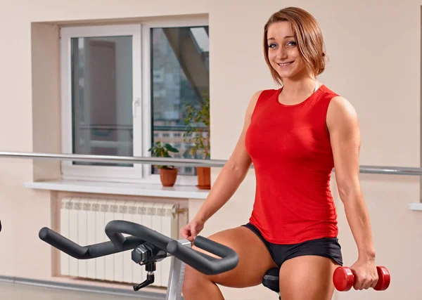 young woman doing indoor biking in a fitness club with dumbbells