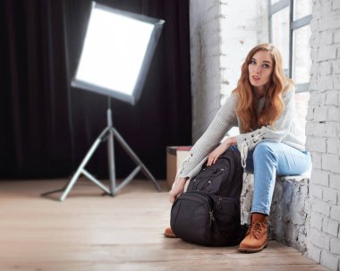 Fotoğraf stüdyosunda, çantasını ekipmanla birlikte boşaltan profesyonel kadın fotoğrafçının portresi. Uzman kadın lensçi profesyonel fotoğraf atölyesindeki kamera ekipmanlarını ortaya çıkardı.