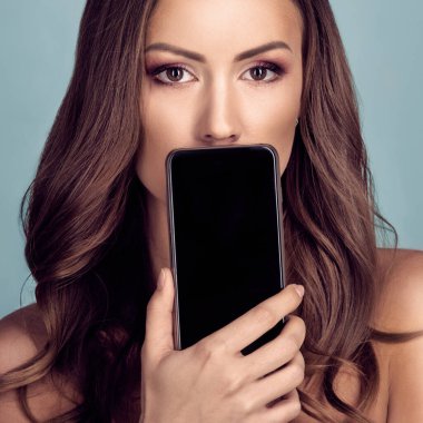 Modern akıllı telefonla ağzını kapatan çekici bir kadının portresi.