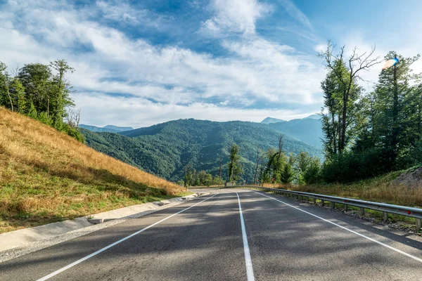 Asphalt mountain road. Blue sky with white clouds.