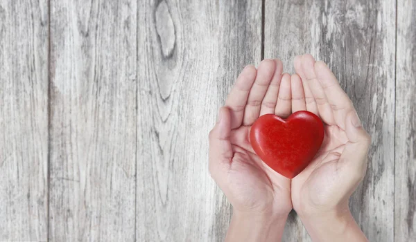 Manos que sostienen el corazón rojo, la salud del corazón y el concepto de donación — Foto de Stock